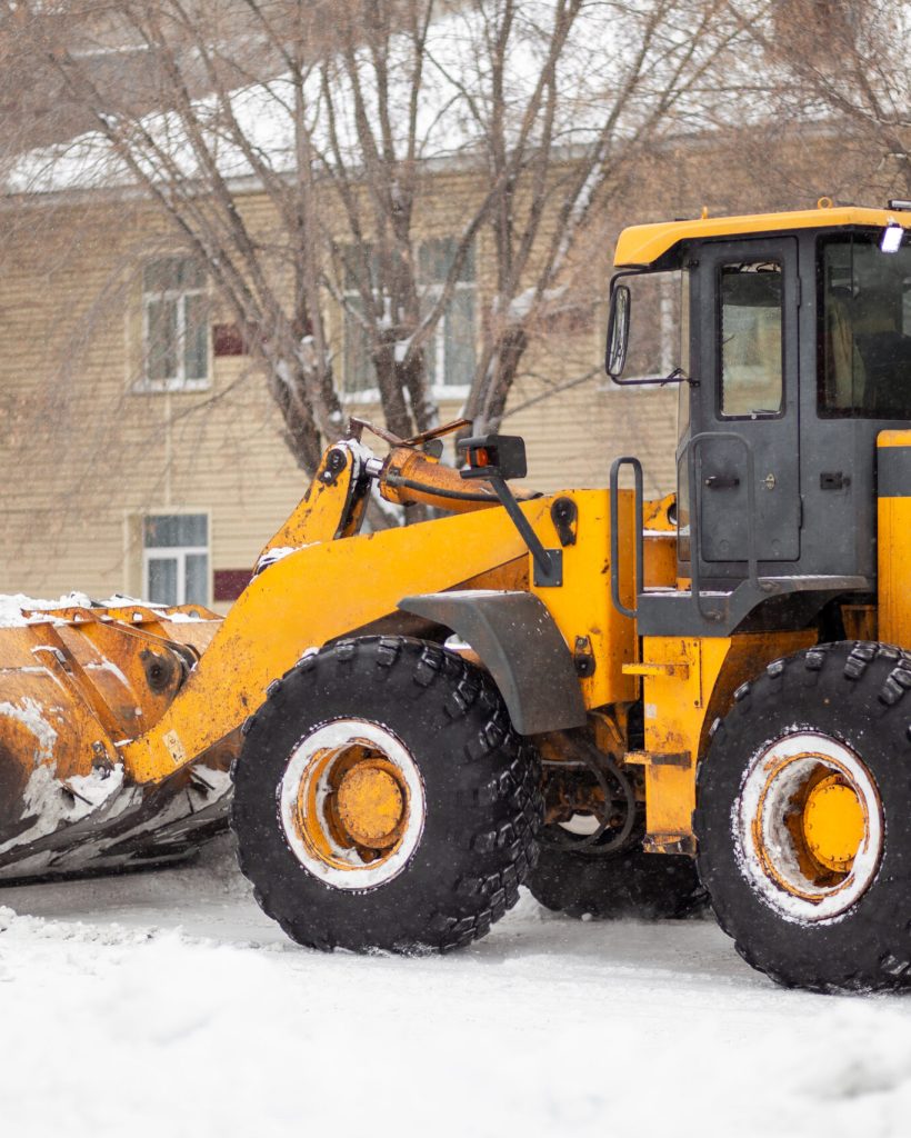 Cleaning and cleaning of roads in the city from snow in winter Orange tractor cleans up snow from the road and loads it into the truck. Cleaning and cleaning of roads in the city from snow in winter. Snow removal after snowfall and blizzards.